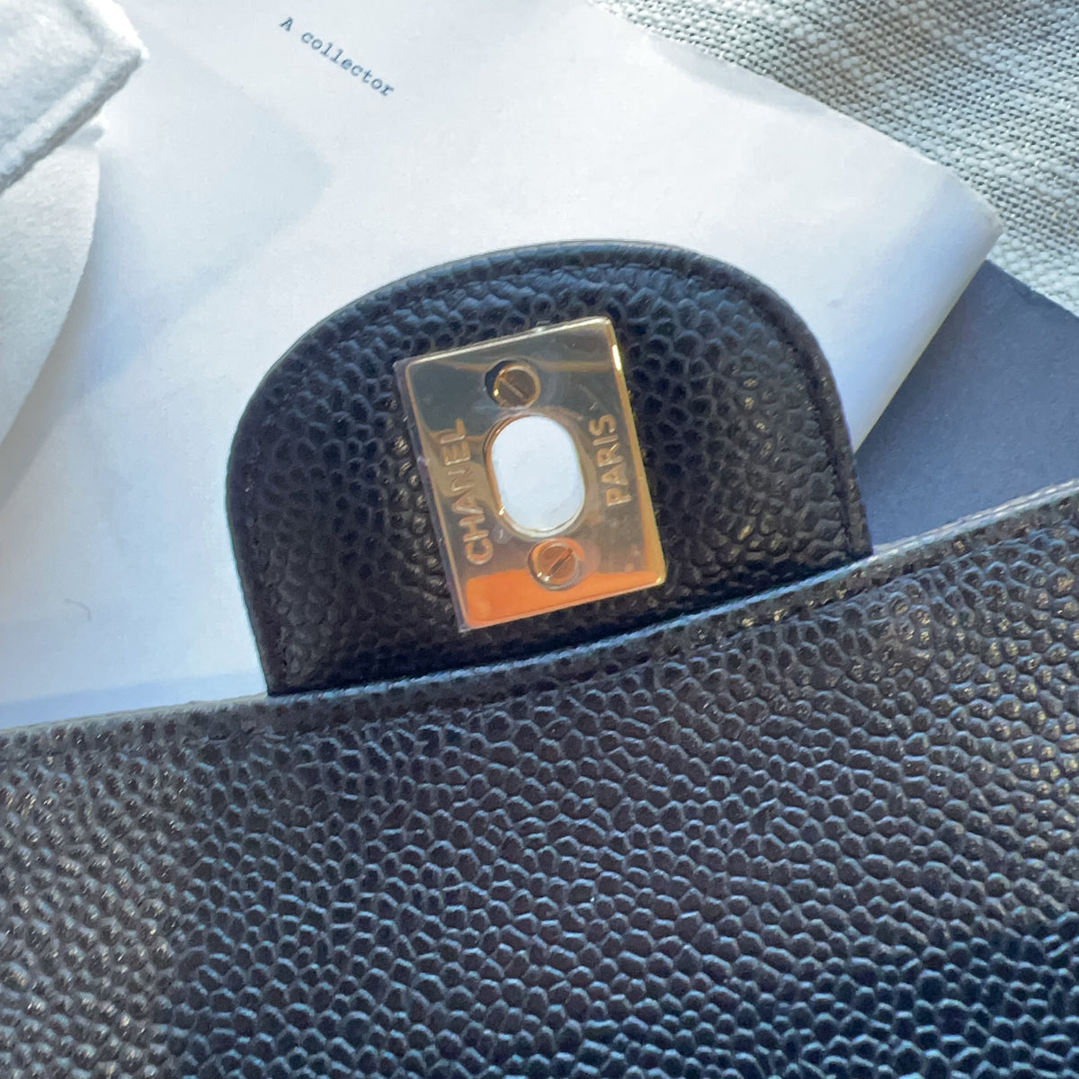 Close-up of a black pebbled leather clutch or wallet showing a gold-tone metal turn-lock closure engraved with 'CHANEL PARIS'.