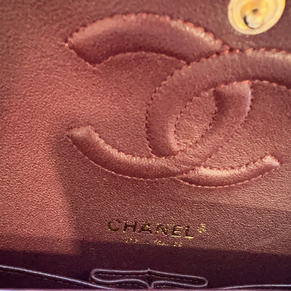 Close-up of a brown textured leather item featuring an embossed Chanel logo and the CHANEL name printed below, with a small gold circular detail in the top right corner.