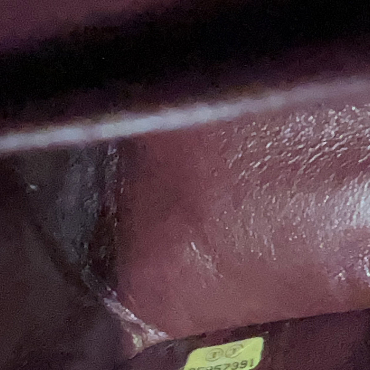 A close-up view of a textured, glossy reddish-brown surface with a small yellow sticker at the bottom edge.