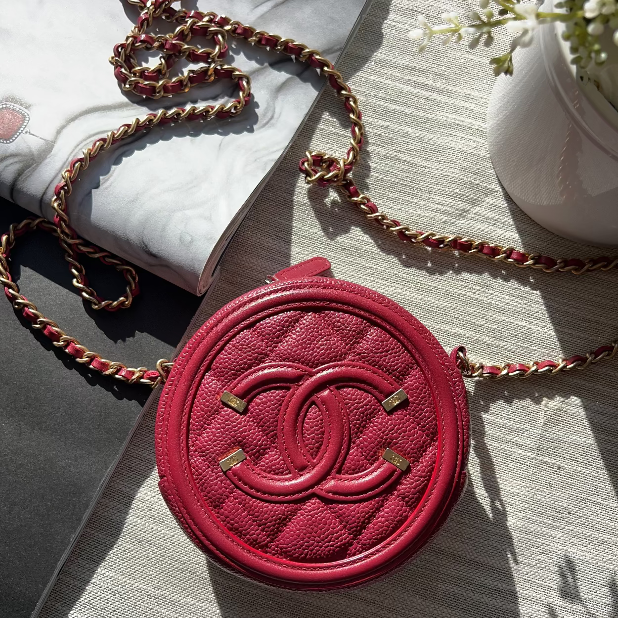 Red round handbag with chain strap on a textured surface