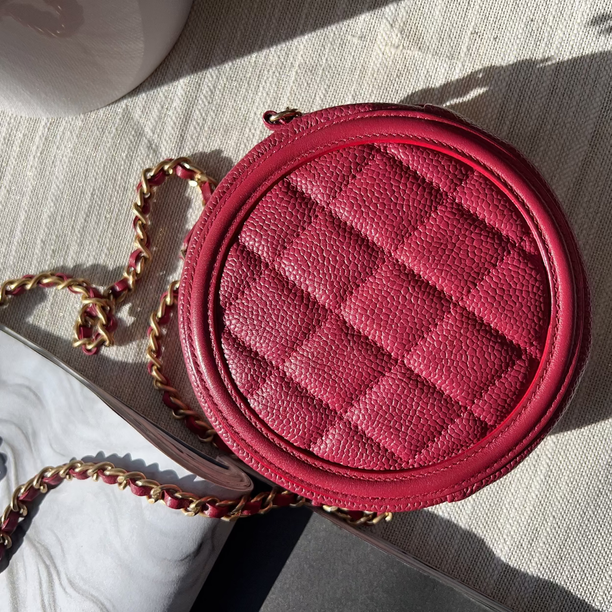 Red quilted handbag with a chain strap on a textured surface