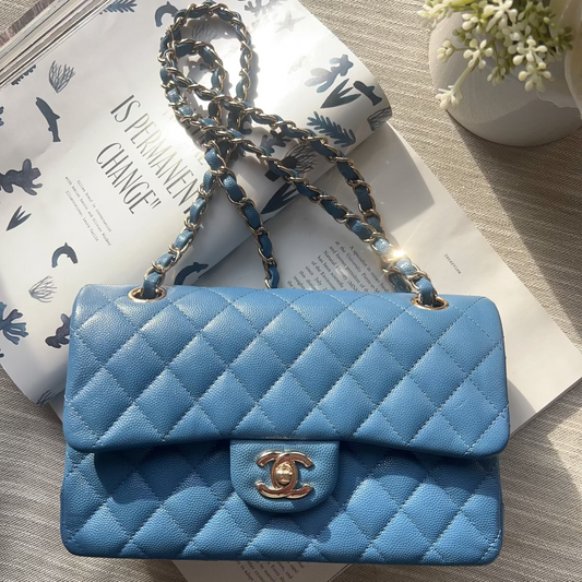 Blue quilted handbag with gold clasp on a light wooden surface with a magazine underneath