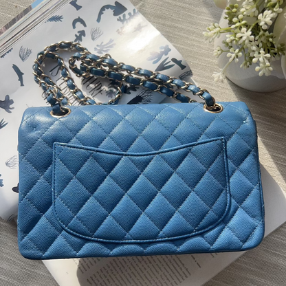 Blue quilted handbag with a chain strap on a surface with a magazine and flowers.