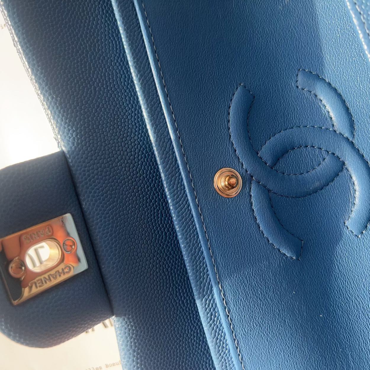Close-up of a blue Chanel handbag with gold hardware on a patterned background