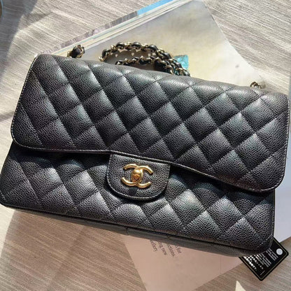 A black quilted leather handbag with a gold-tone interlocking CC clasp, resting on a light-colored surface with its original paper tag and packaging visible.