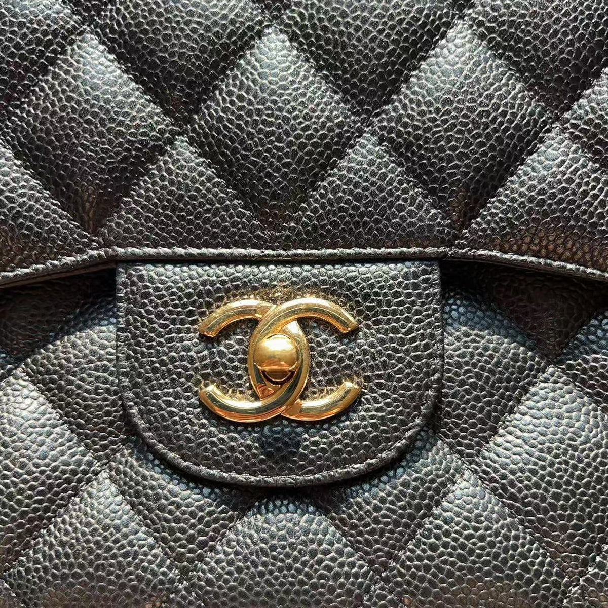 Close-up of a black quilted leather handbag with a gold-tone interlocking CC logo clasp on a flap pocket.