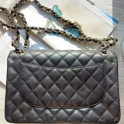 A black quilted leather shoulder bag with a gold-tone chain strap, laid flat on a light-colored wooden surface next to a magazine.