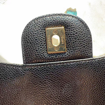Close-up of a dark brown pebbled leather handbag showing a gold-tone metal clasp with the brand name 'CHANEL' and 'PARIS' engraved on it.
