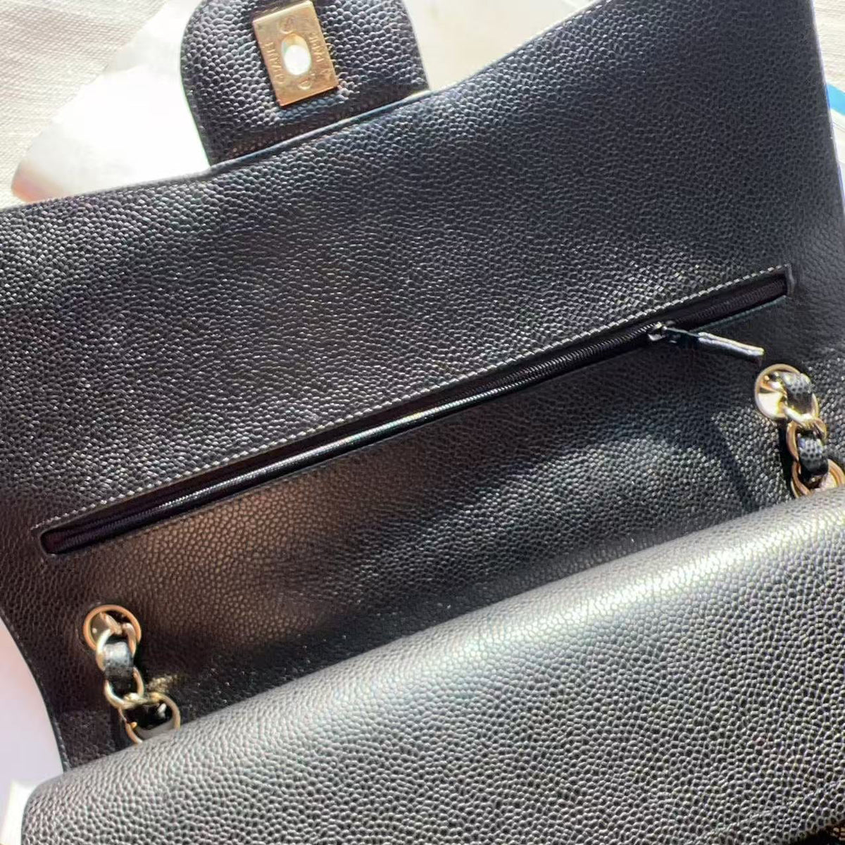 Close-up of a black pebbled leather handbag showing the interior pocket with a zipper, gold-tone hardware, and part of a quilted exterior.