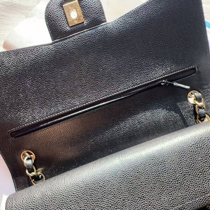 Close-up of a black pebbled leather handbag showing the interior pocket with a zipper, gold-tone hardware, and part of a quilted exterior.