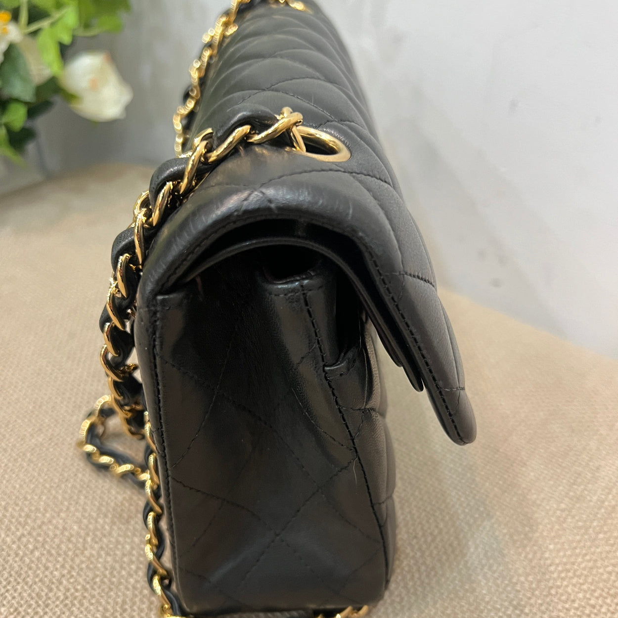 Black quilted handbag with gold chain detail on a beige surface