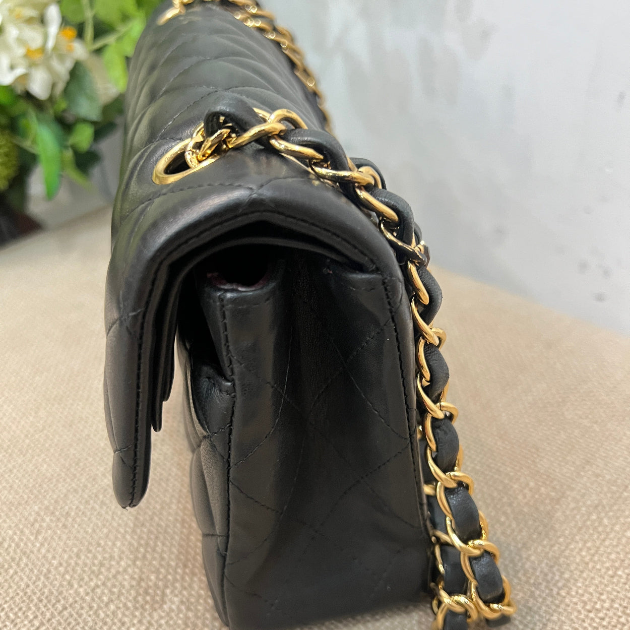Black handbag with gold chain strap on a mannequin against a neutral background