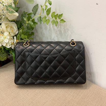 Black quilted handbag on a beige surface with flowers in the background