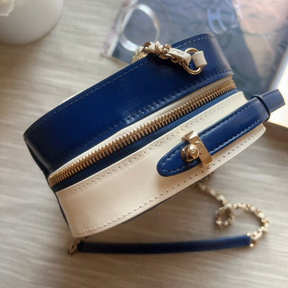 Blue and beige handbag with gold zipper and hardware on a light wooden surface.