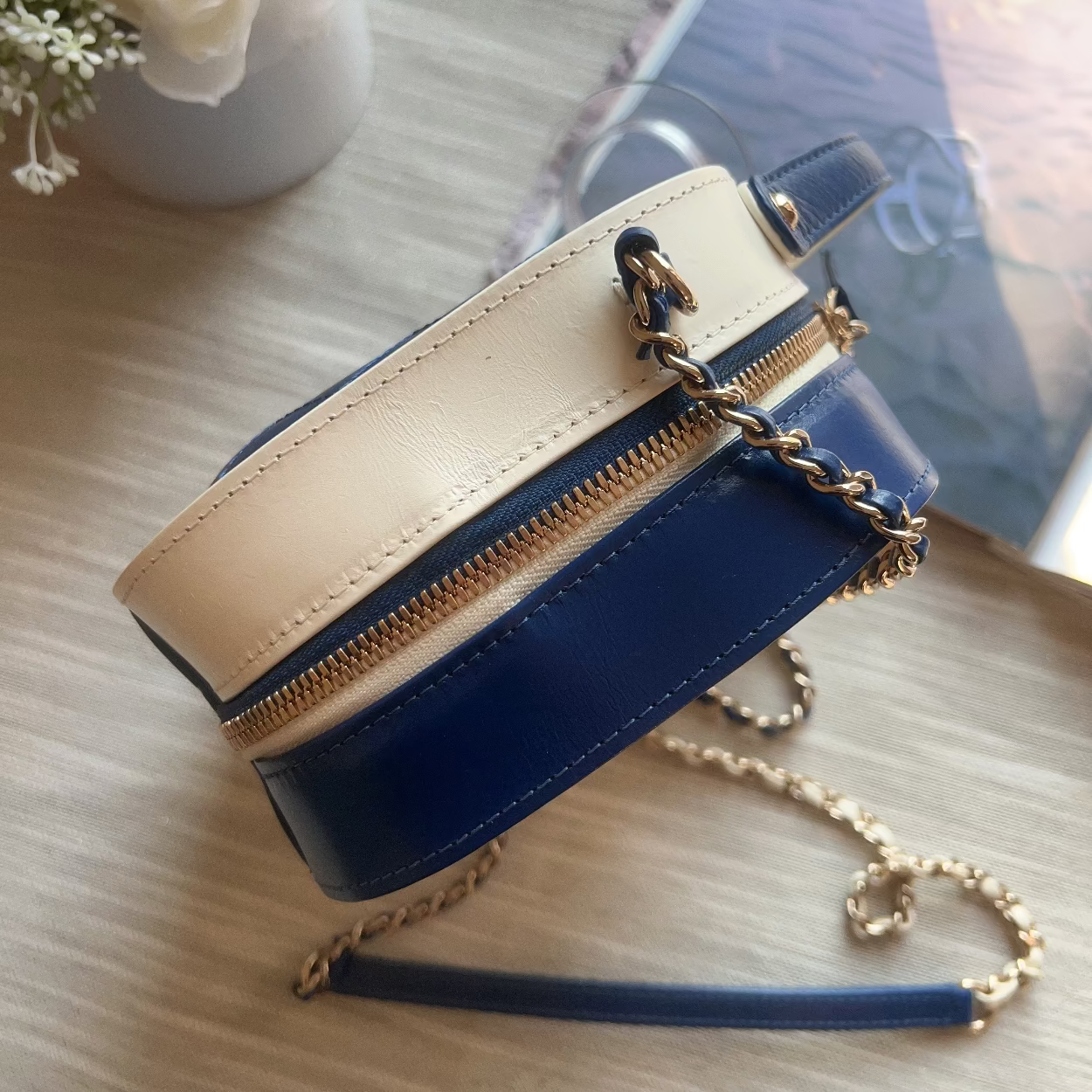 Blue and beige handbag with a gold chain on a light wooden surface.