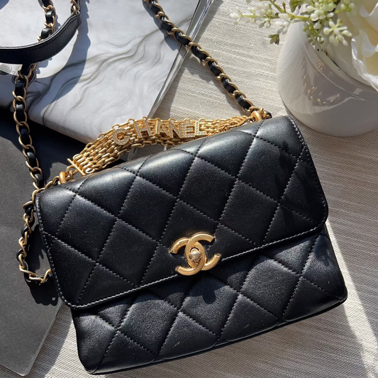 Black quilted handbag with gold chain strap on a light wooden surface.