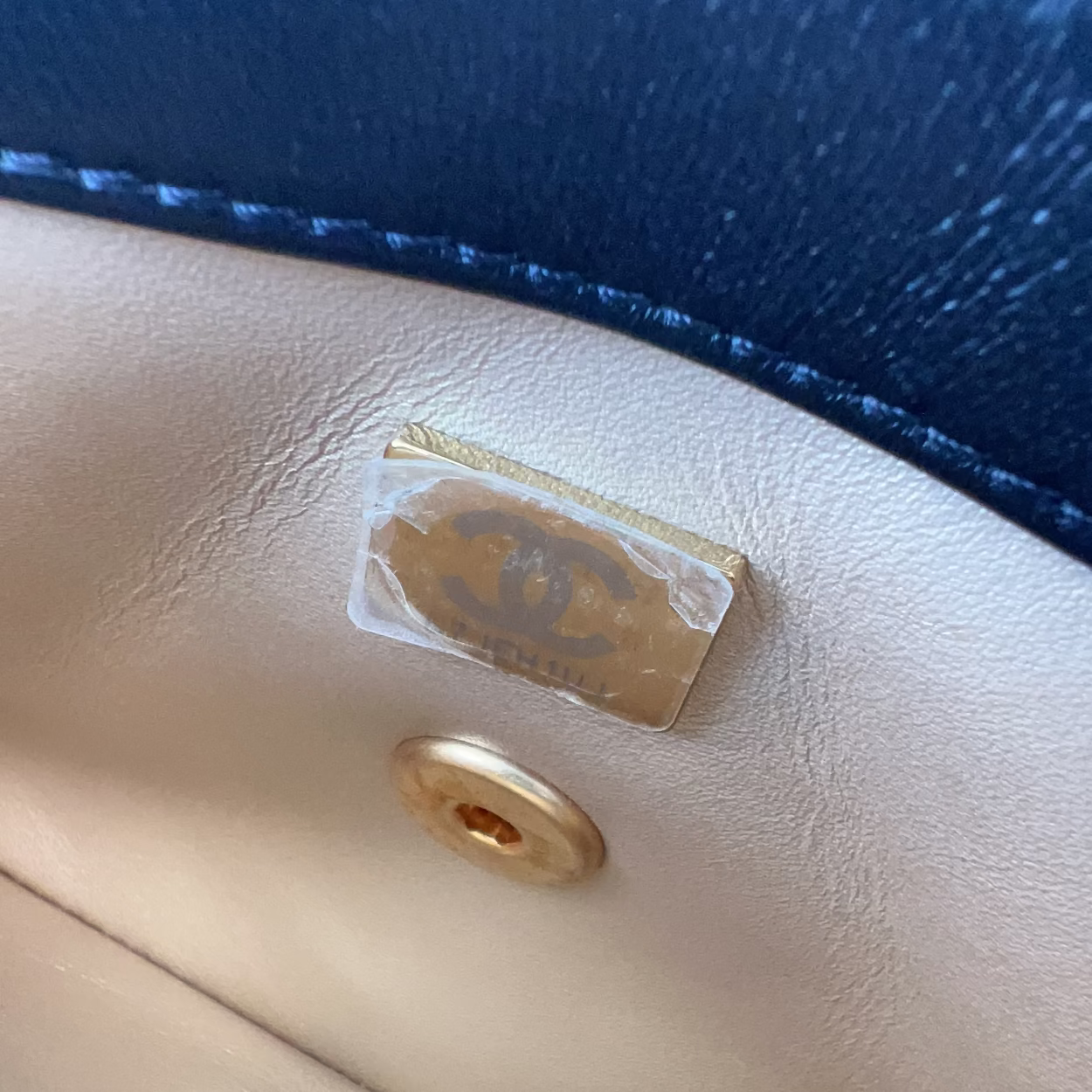 Close-up of a Chanel logo tag on a beige handbag with a blue background.