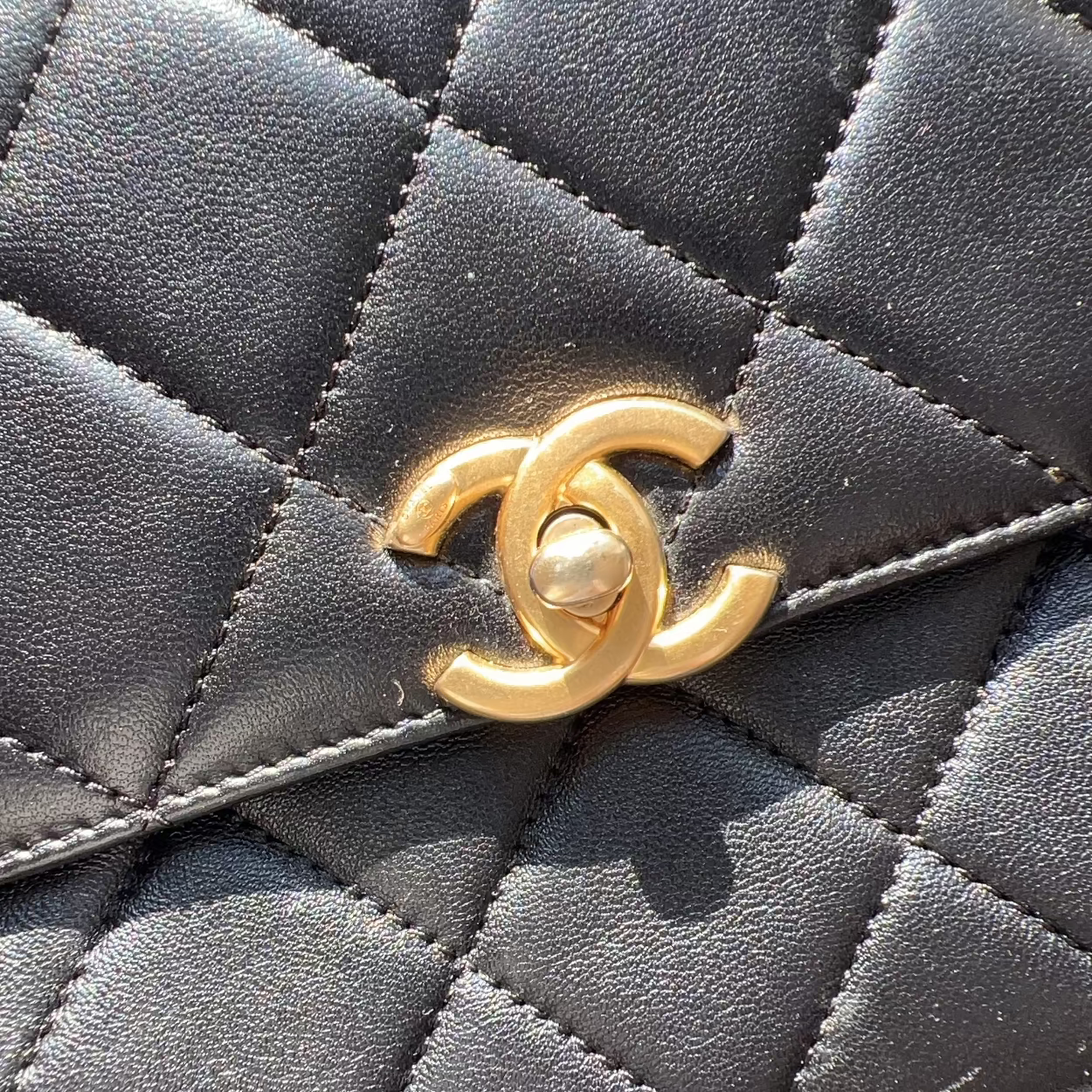 Close-up of a Chanel handbag with a gold CC logo on a textured surface.