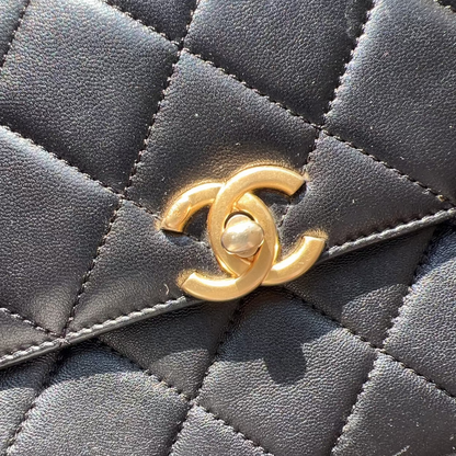 Close-up of a Chanel handbag with a gold CC logo on a textured surface.