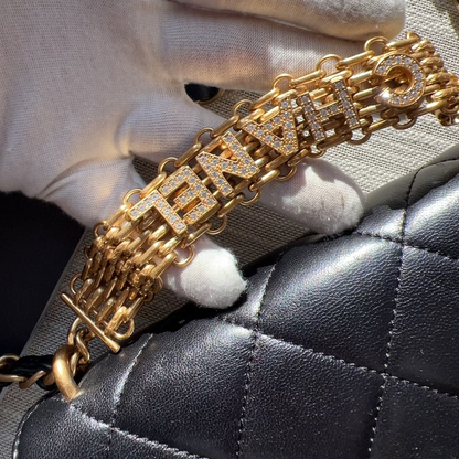 Gold bracelet with 'FENDI' branding held by a hand against a black quilted surface.