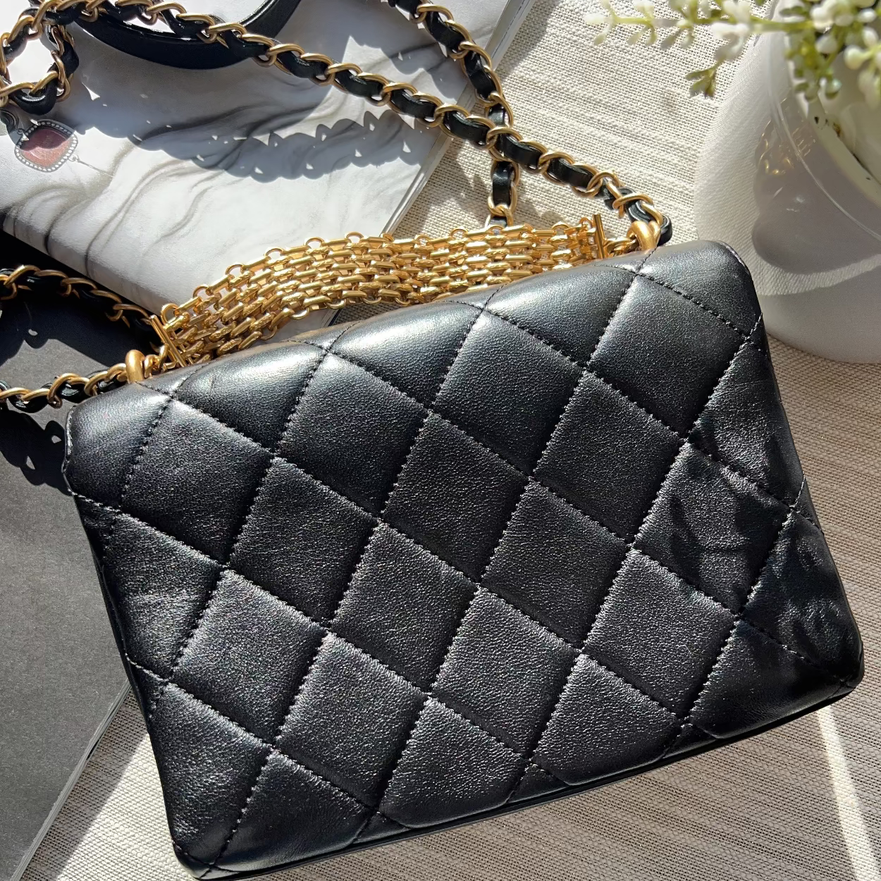 Black quilted handbag with gold chain strap on a light wooden surface