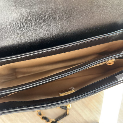 Close-up of a black leather handbag with gold hardware on a light wooden surface.