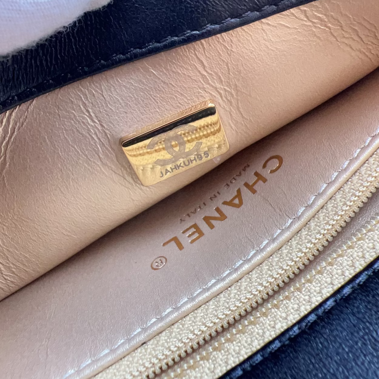 Close-up of a Chanel wallet or card case interior showing a beige leather lining with gold-tone hardware, a black leather edge, and the CHANEL name printed on the inside.