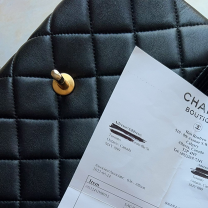 A black quilted Chanel handbag with gold-tone hardware lies on a light beige fabric surface, with a branded Chanel Boutique receipt sheet placed on top.