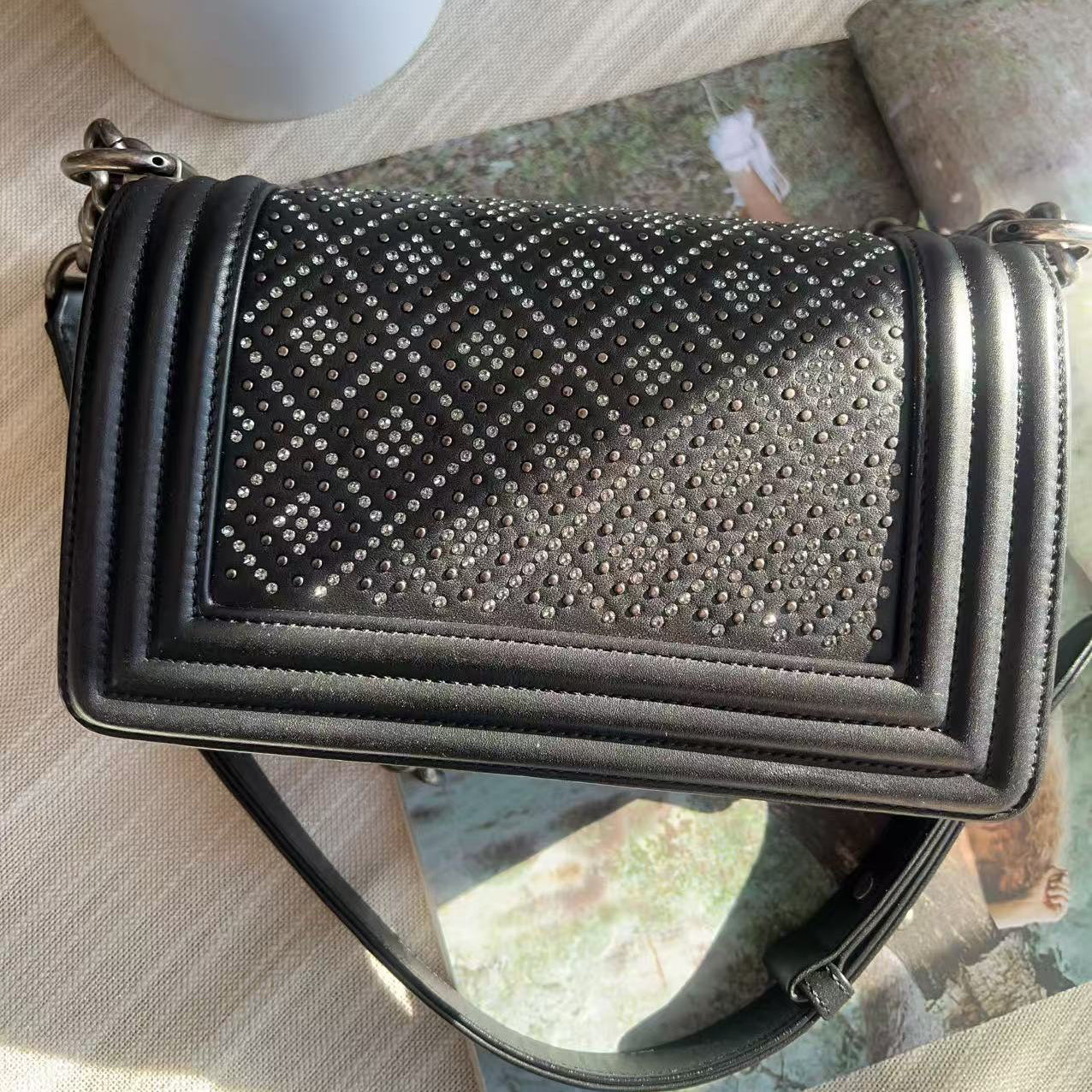 Black studded handbag on a reflective surface with a blurred background
