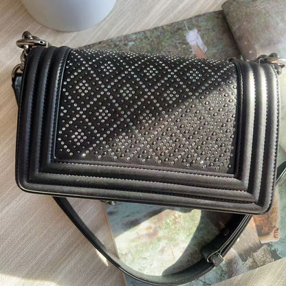 Black studded handbag on a reflective surface with a blurred background
