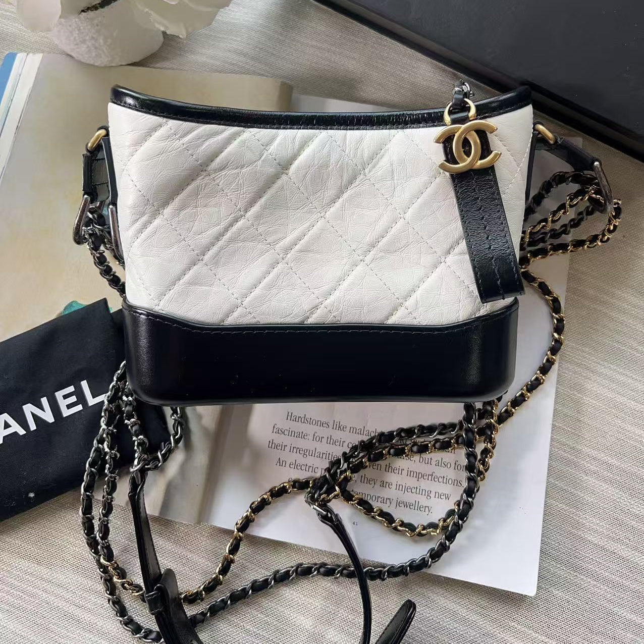 White quilted handbag with black strap and chain detail on a light wooden surface.