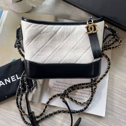 White quilted handbag with black strap and chain detail on a light wooden surface.