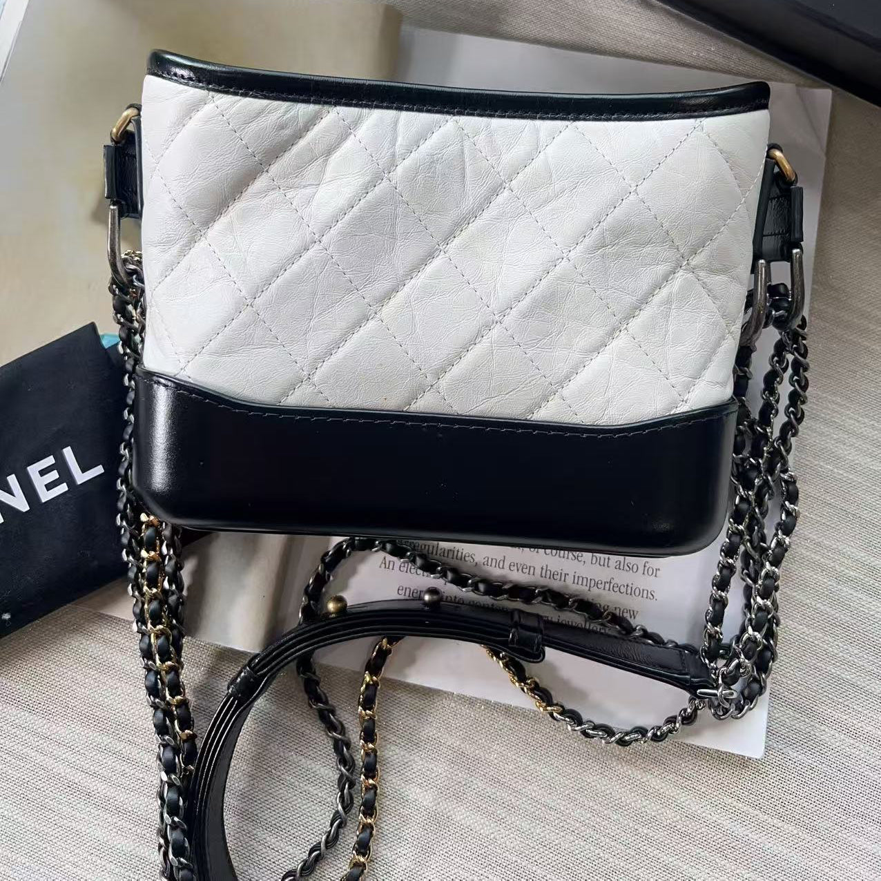 White quilted handbag with black accents and a chain strap on a light gray surface.