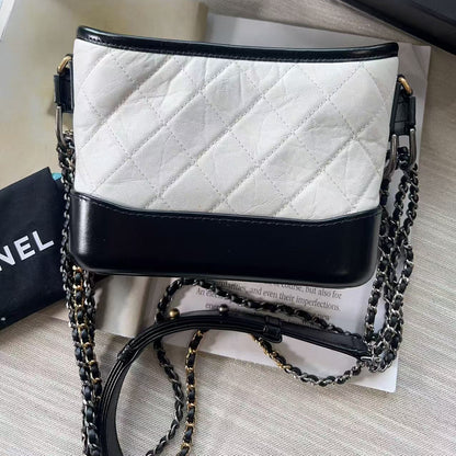 White quilted handbag with black accents and a chain strap on a light gray surface.
