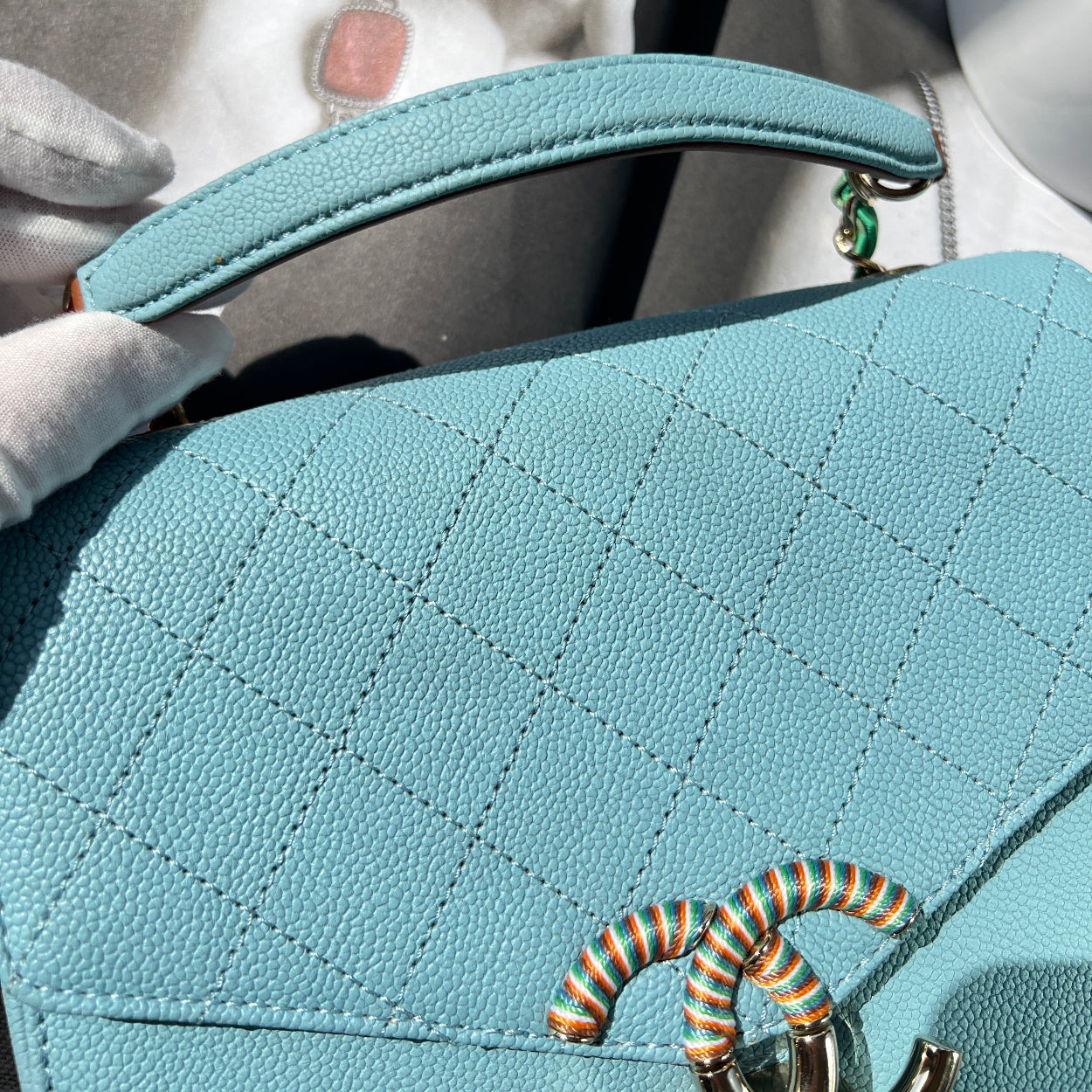 Close-up of a light blue handbag with decorative elements, held by a person wearing white gloves.
