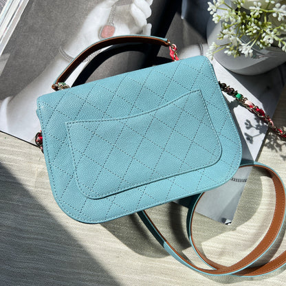 Light blue quilted handbag with black handle on a textured surface with flowers and books.