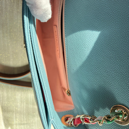 Light blue handbag with gold chain handle held by a gloved hand.
