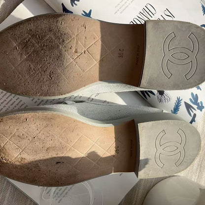 A pair of Chanel slip-on shoes shown from the sole, with the iconic interlocking CC logo embossed on the heel. The soles are heavily stained and worn down, and the shoes rest on a patterned magazine page over a neutral fabric surface.