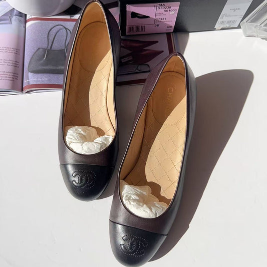 Pair of black Chanel shoes on a white surface with a magazine and plant in the background.