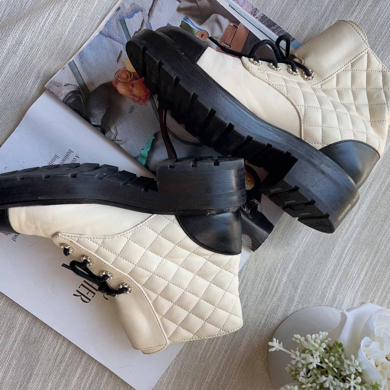 Pair of beige quilted shoes with black soles on a textured surface.
