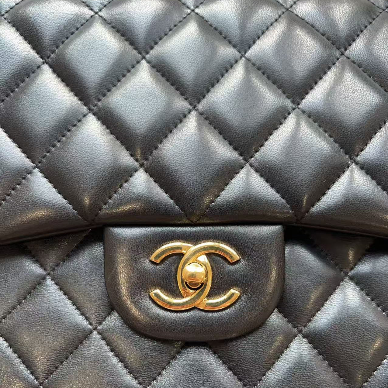 A close-up of a black quilted leather handbag with a gold-tone interlocking CC logo clasp, showing the signature diamond pattern and textured leather.