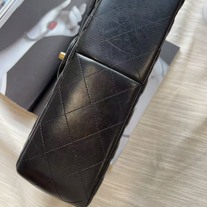A black quilted leather handbag with gold-tone hardware, photographed from an overhead angle resting on a magazine over a light wood surface.