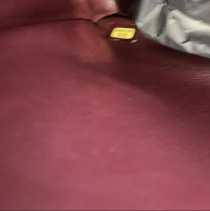 A close-up view of a burgundy leather interior, showing a small gold rectangular hardware piece next to a crumpled silver-gray fabric.