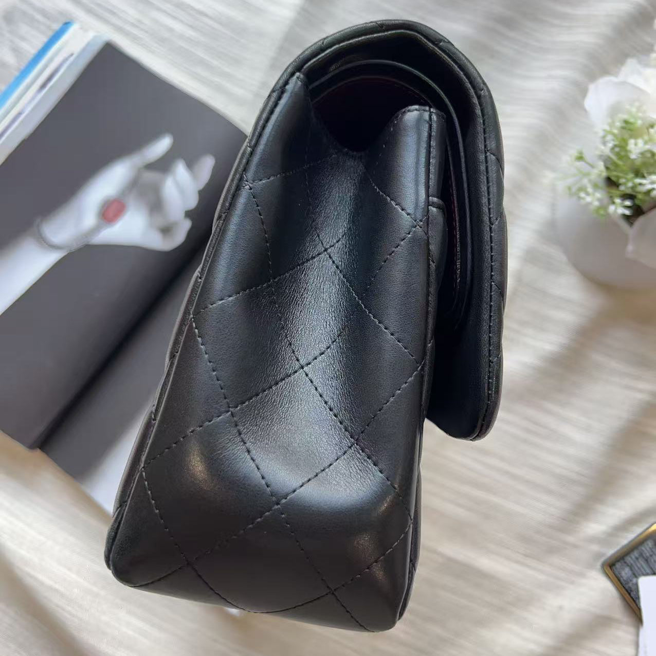 A black quilted leather shoulder bag with a structured, slouchy silhouette, photographed from an overhead angle on a light beige fabric surface with styled props.