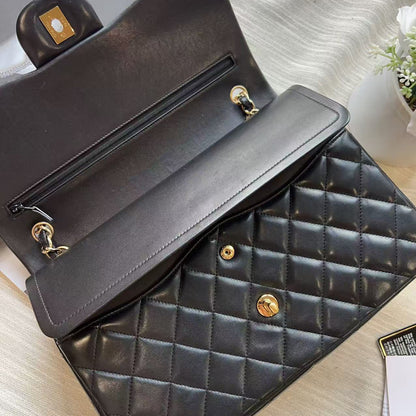 A black quilted leather handbag shown open, revealing a zippered interior and gold-tone hardware, photographed on a light wood surface with a neutral fabric backdrop.