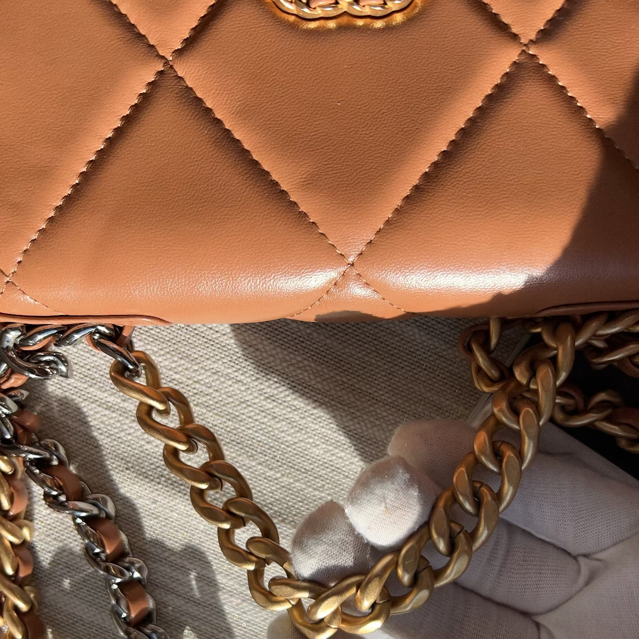 Close-up of a brown quilted handbag with gold chain strap on a textured surface.