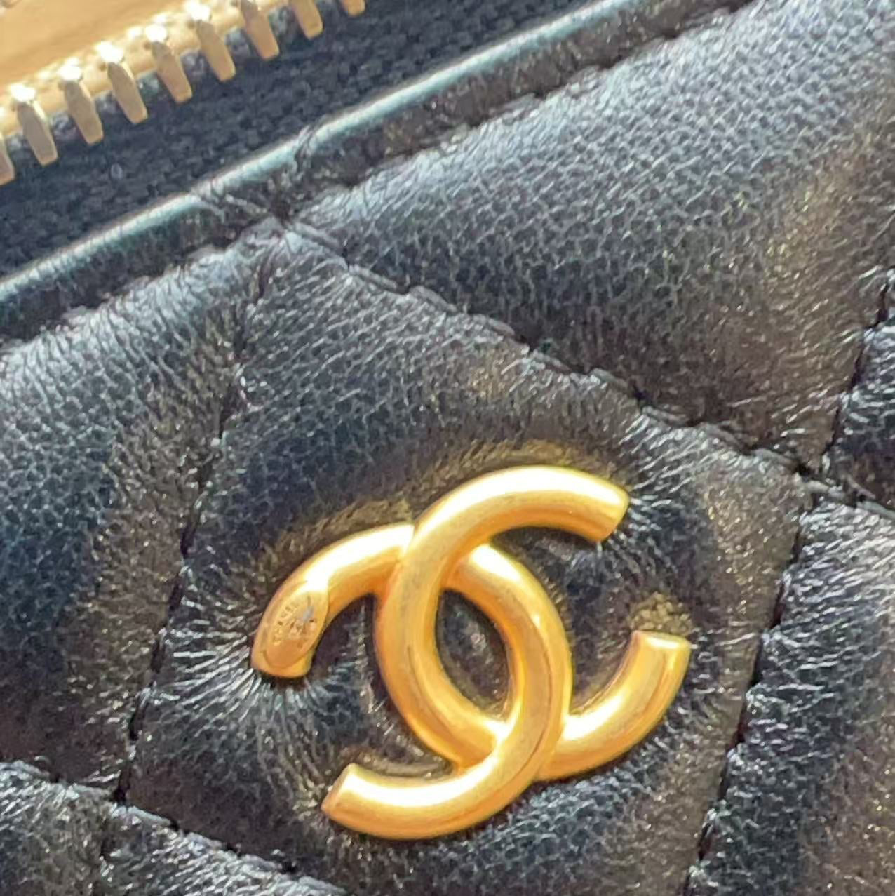 Close-up of a black quilted leather item featuring a prominent gold-tone interlocking CC logo, characteristic of Chanel.