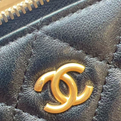 Close-up of a black quilted leather item featuring a prominent gold-tone interlocking CC logo, characteristic of Chanel.