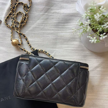 A black quilted leather Chanel shoulder bag with gold-tone chain strap, resting on a black dust bag over a textured beige fabric background.