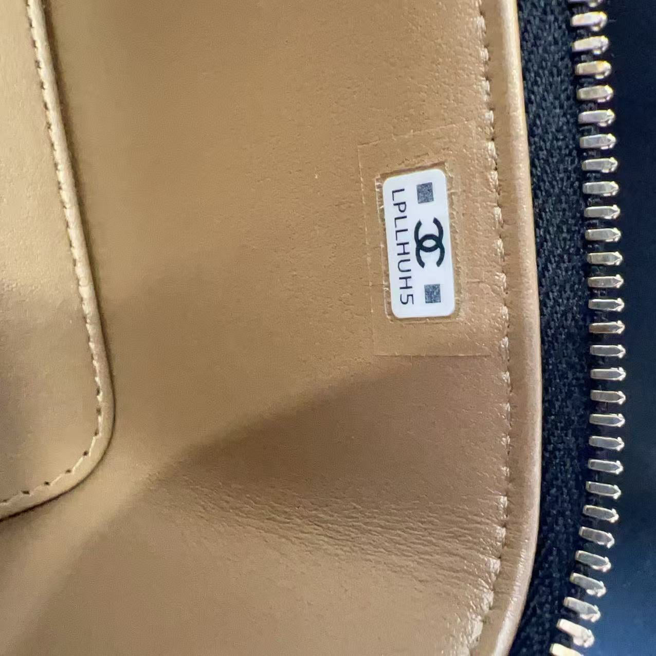 Close-up of a beige leather zipper pouch with a white Chanel PLHJUH5 label, next to a black canvas zipper track.